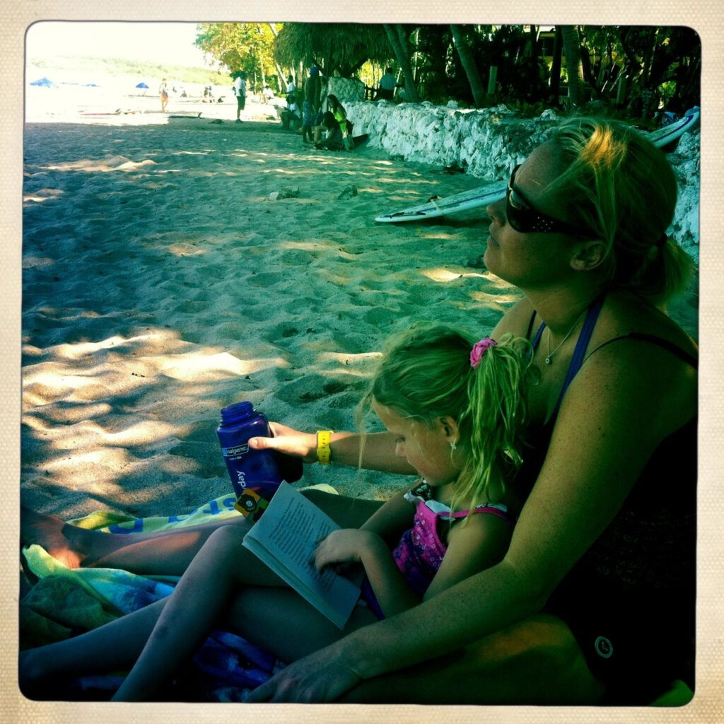 Erin and Abby Sampson reading in the shade on Tamarindo beach with a water bottle